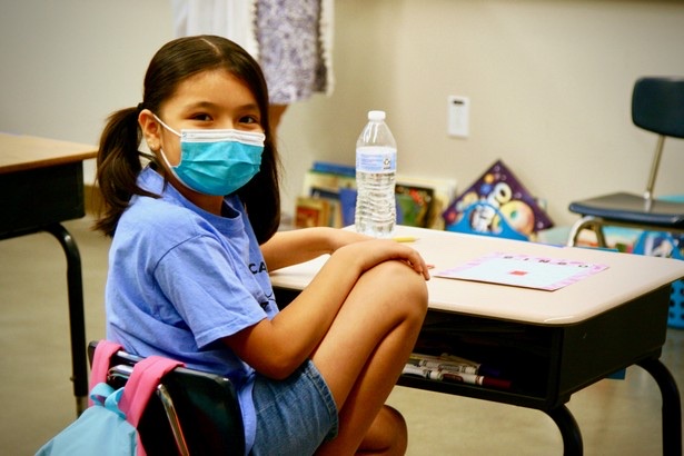 A masked Learning Academy student seated at her desk
