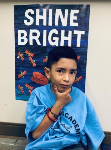 A Learning Academy student in front of a "Shine Bright" classroom poster, 2022