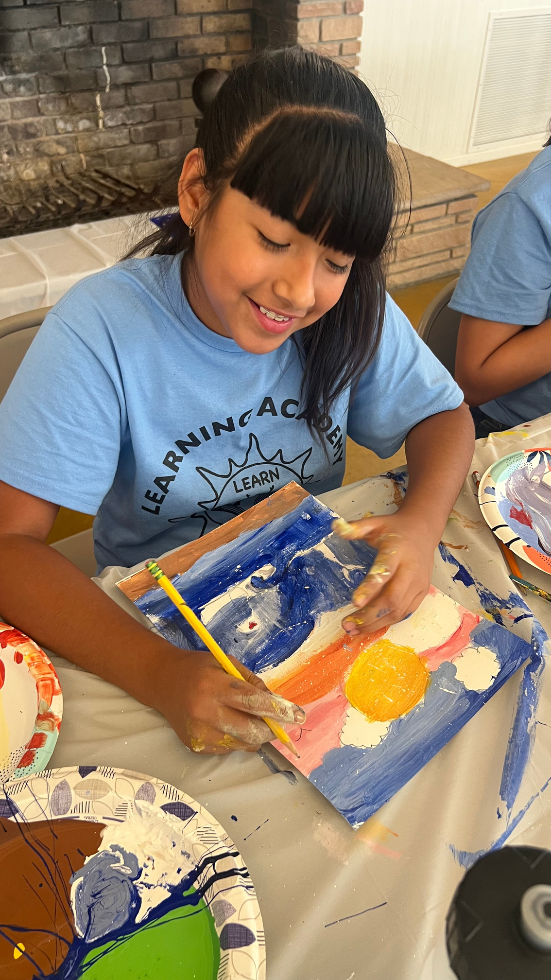A Learning Academy student painting a sun and desert scene