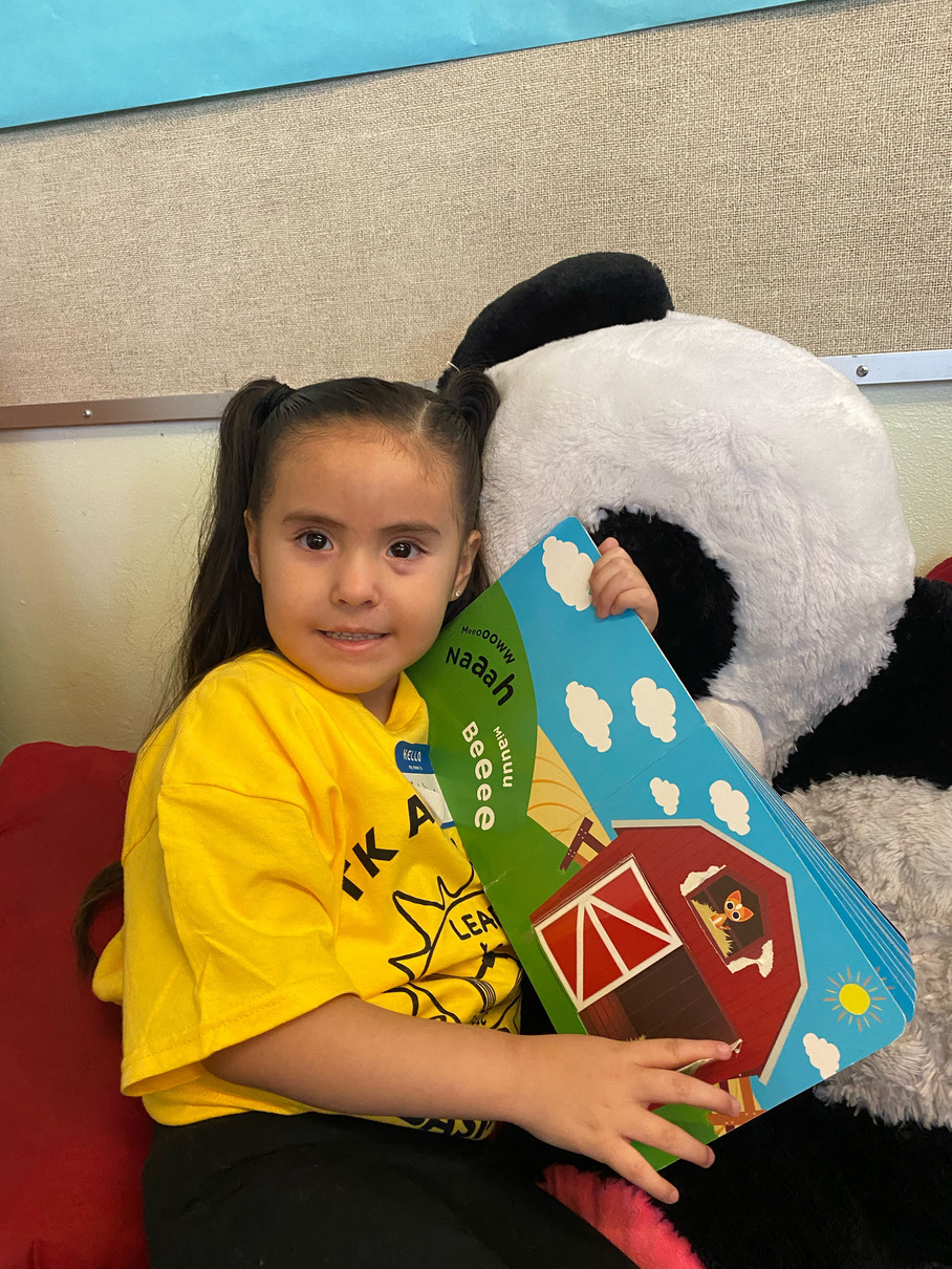 A TK Academy student sitting with a picture book and a large stuffed panda