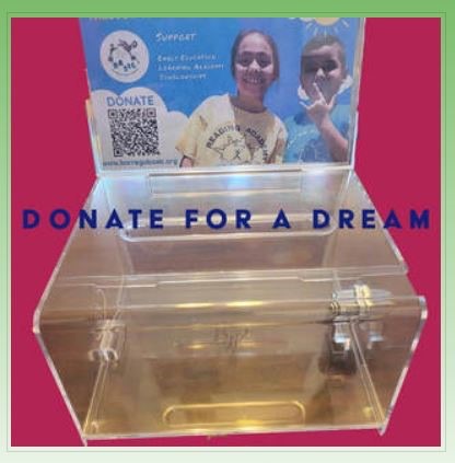 A clear acrylic BASIC donation box with a Donate for a Dream card showing two smiling students