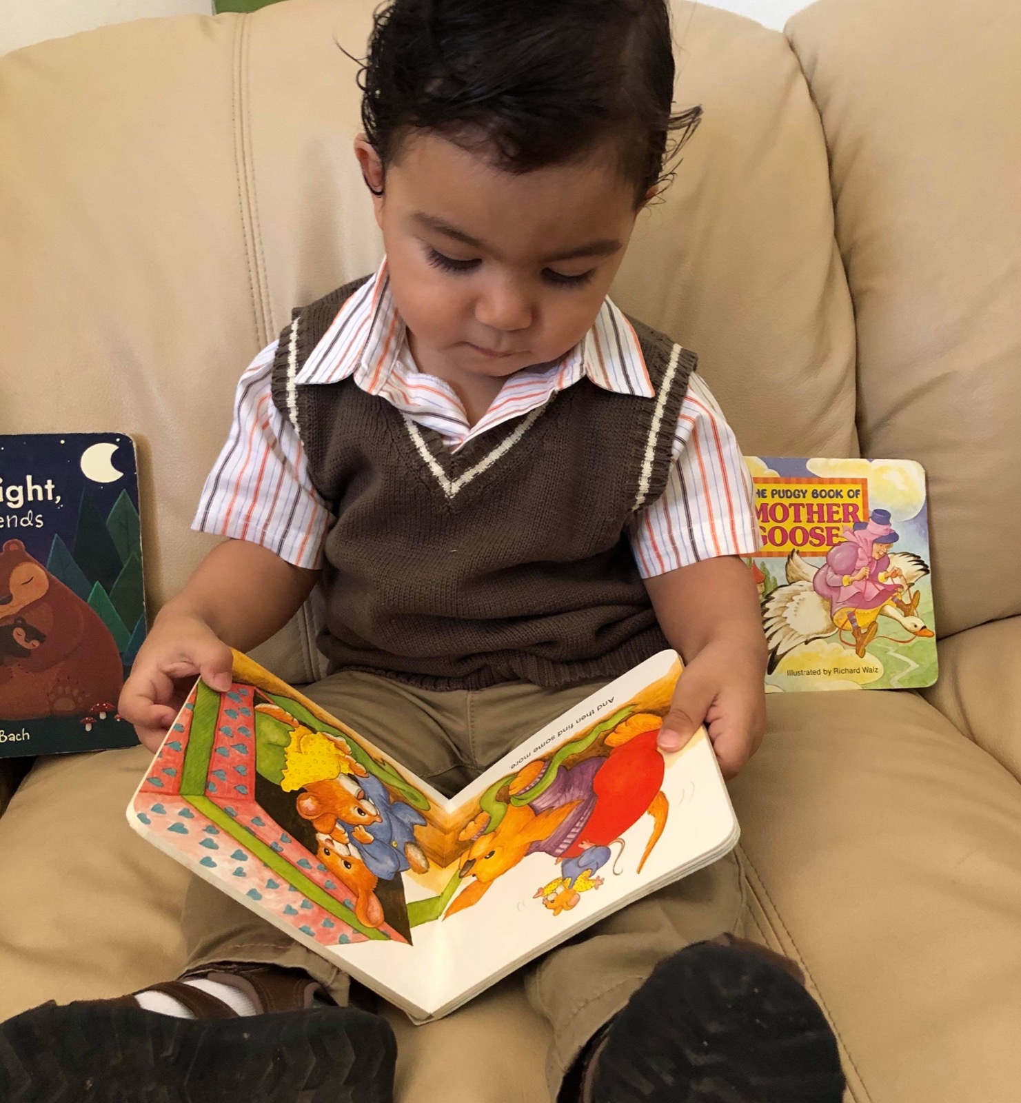 Dylan Garcia as a toddler in a sweater vest, holding an open board book