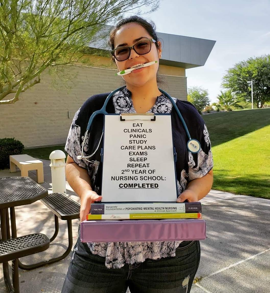 Jamie Blakeley holding a sign reading Eat, Clinicals, Panic, Study, Care Plans, Exams, Sleep, Repeat: 2nd year of nursing school completed