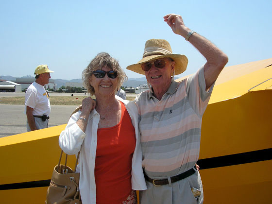 Bill and Jenny Wright waving beside a yellow aircraft at the Borrego Valley Airport