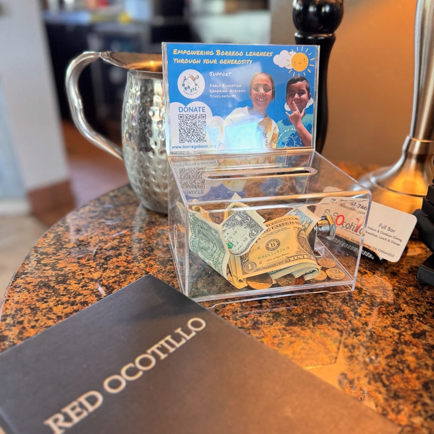 The BASIC donation box on the counter at Red Ocotillo, holding several folded bills