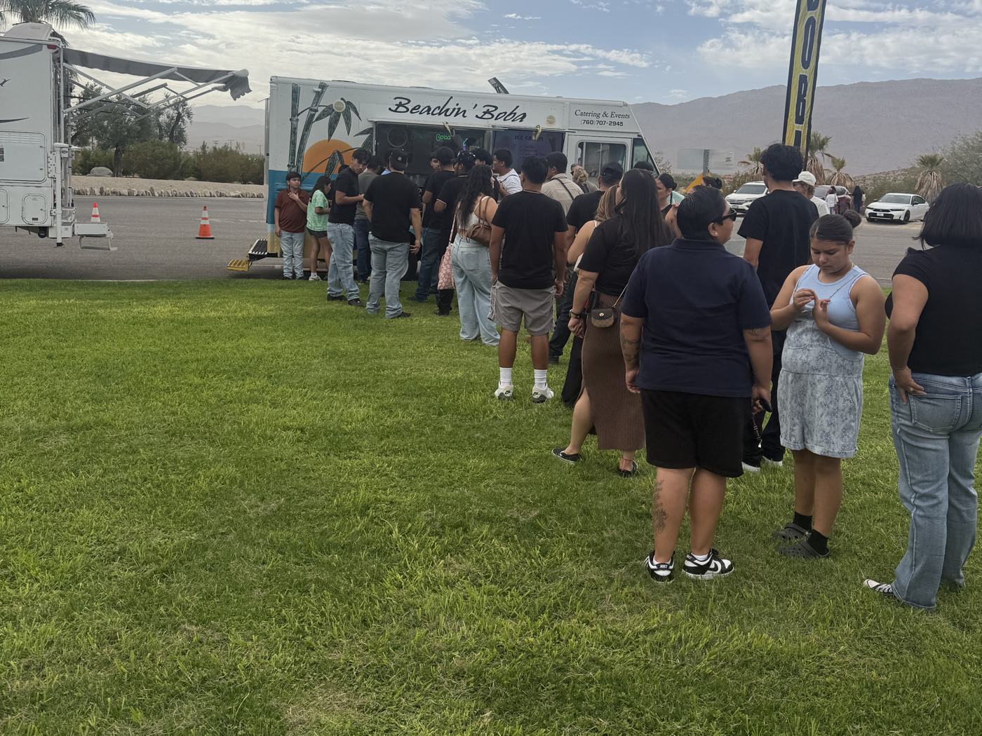 A long line of festival-goers across the grass waiting at the Beachin' Boba truck under an overcast sky