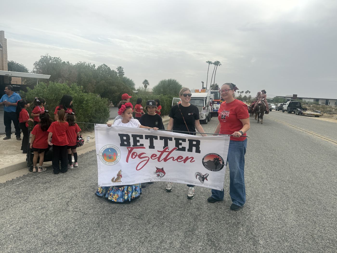 Borrego Springs Unified School District students and staff in red shirts holding a Better Together banner at the parade lineup, with K-12 Principal Victoria Baay among them