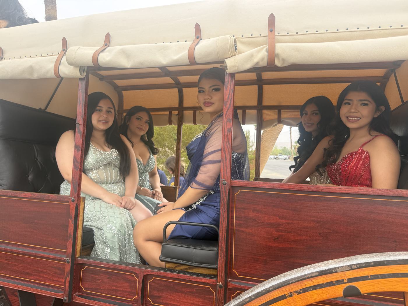 Five Miss Borrego Springs contestants in evening gowns seated inside a red wooden stagecoach, smiling through the open window