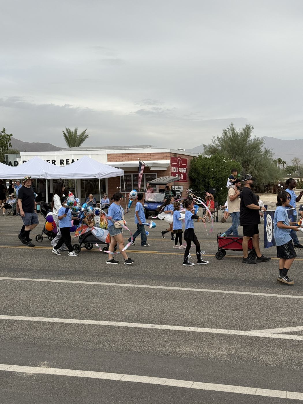 Learning Academy students in blue shirts crossing the street in the parade with balloons and a red wagon